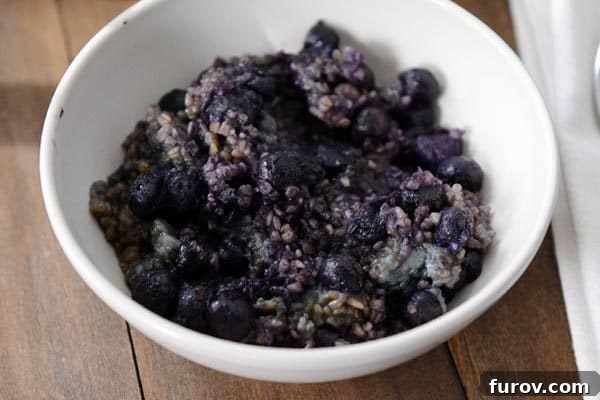 Hearty Blueberry Almond Baked Steel Cut Oats 3 A white bowl full of blueberry filled cooked steel cut oats.