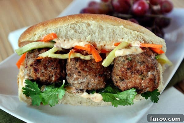 A beautifully presented meatball Banh Mi sub sandwich on a white plate, ready to be enjoyed.