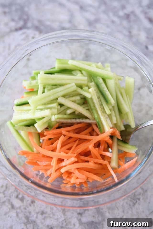 Glass bowl filled with freshly shredded carrots and cucumbers, ready for pickling.