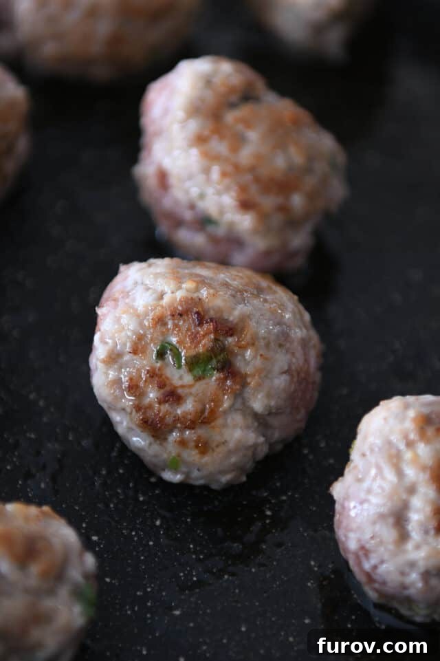 Close-up of a cooked, browned meatball sizzling in a hot skillet with sesame oil.