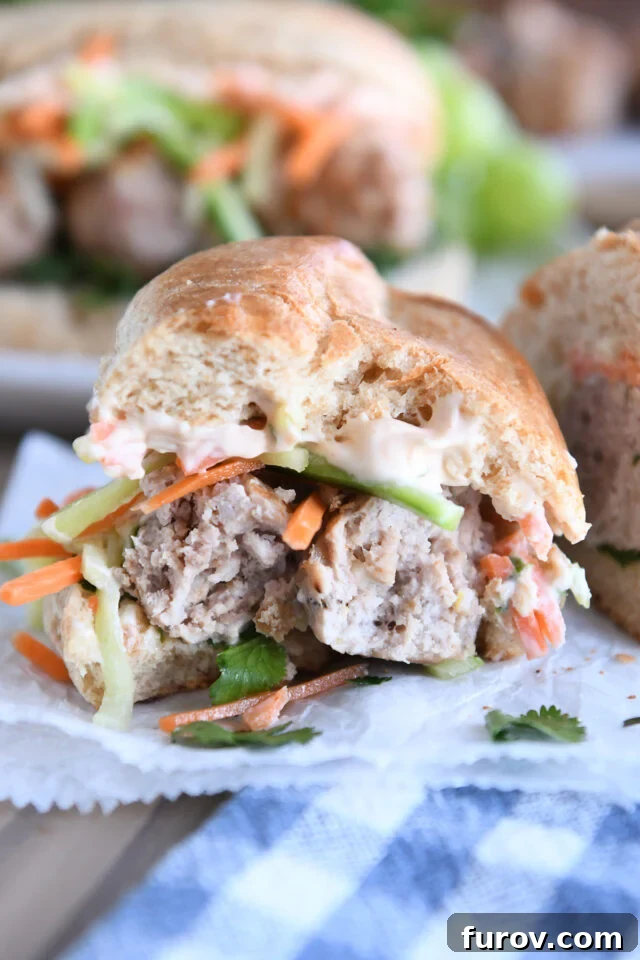 A half-eaten Banh Mi meatball sub on parchment paper, showcasing the delicious layers inside.