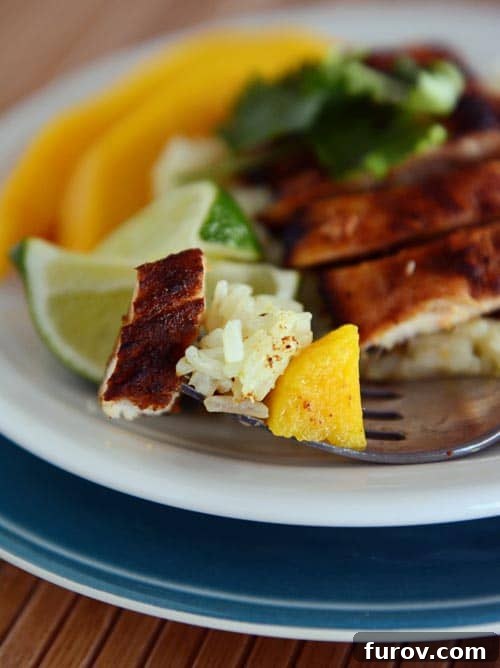 One-Pan Sweet Paprika Chicken 3 A beautifully arranged white plate with golden sweet paprika skillet chicken slices, fresh mango pieces, a wedge of lime, and a generous portion of cilantro lime rice.