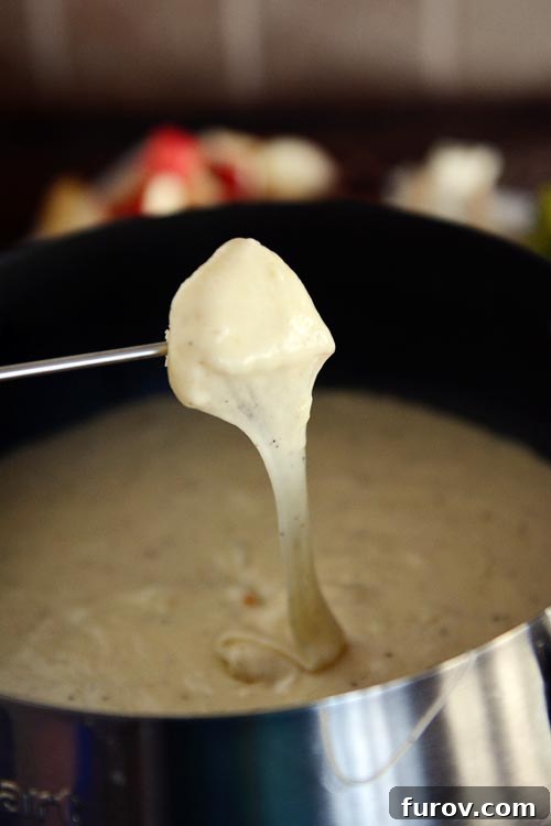 A skewer lifting a piece of food out of a pot of creamy, stretchy cheese fondue, showcasing its perfect consistency.