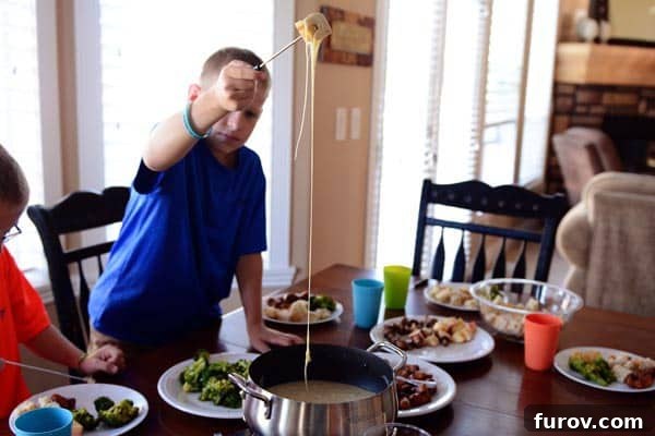 A young boy pulling a piece of bread from a fondue pot, creating a long, impressive string of melted cheese.