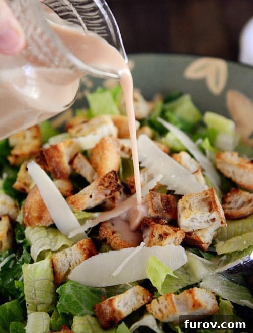 Irresistible Caesar Salad Featuring Homemade Dressing 2 Homemade Caesar dressing being poured generously over a large bowl of crisp romaine lettuce, Parmesan cheese, and golden croutons.