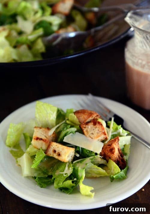 Irresistible Caesar Salad Featuring Homemade Dressing 4 A single serving of Caesar salad with golden croutons and shaved Parmesan on a white plate, ready to be enjoyed.
