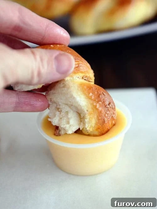 A chunk of homemade pretzel twist being dunked into a luxurious, golden cheese sauce, showcasing its soft interior.