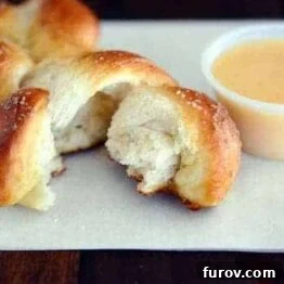 A beautifully baked soft pretzel twist next to a bowl of creamy cheese sauce.