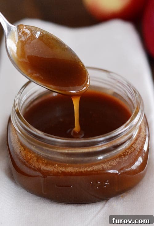 A spoon drizzling rich, golden caramel sauce into a mason jar, showcasing its smooth texture.