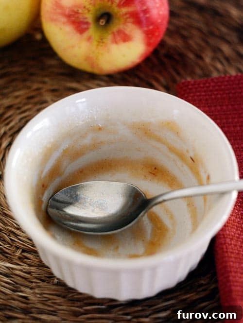 A white ramekin with a spoon and a little bit of applesauce left in it.