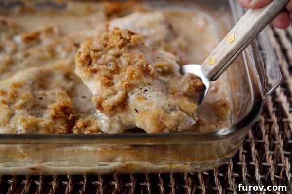Golden Swiss Gratin Chicken 3 A piece of crunchy-topped swiss cheese chicken being lifted by a metal spatula, showing its layers.