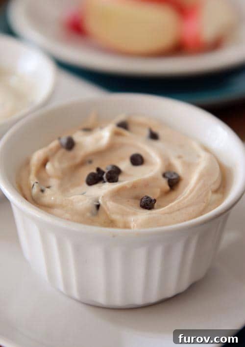 A small white ramekin full of creamy cookie dough dip, topped with a generous sprinkle of mini chocolate chips.