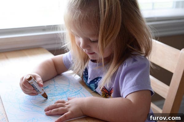 A little girl sitting at a table drawing a picture.