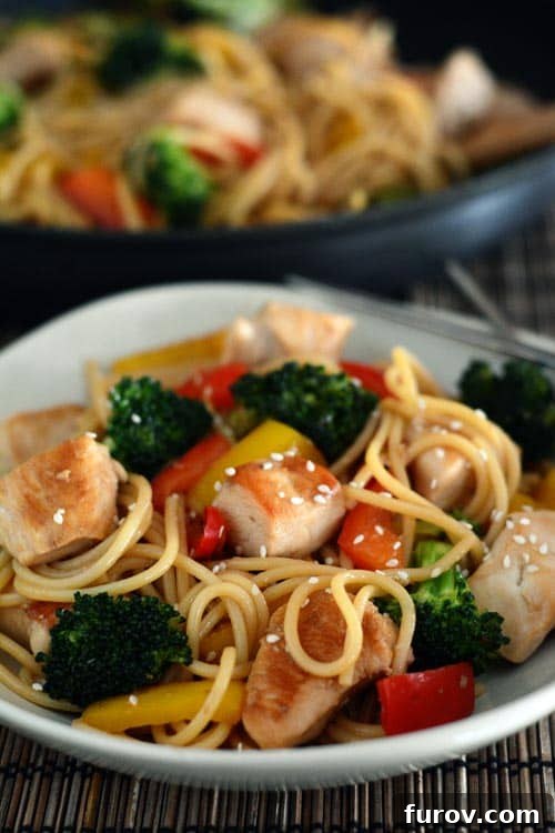 A plate and skillet full of chicken and vegetable lo mein, garnished with sesame seeds.