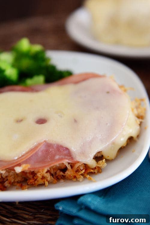 Ham and Swiss Chicken Bake 2 A swiss cheese and ham covered chicken breast on a white plate.