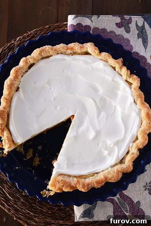 An overhead view of a whole Apple Cheesecake Pie with a slice removed, revealing the beautifully layered texture and a creamy whipped topping, ready to be served and enjoyed.