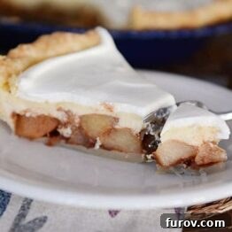 A close-up of a slice of Apple Cheesecake Pie with a fork, showcasing the creamy and apple layers
