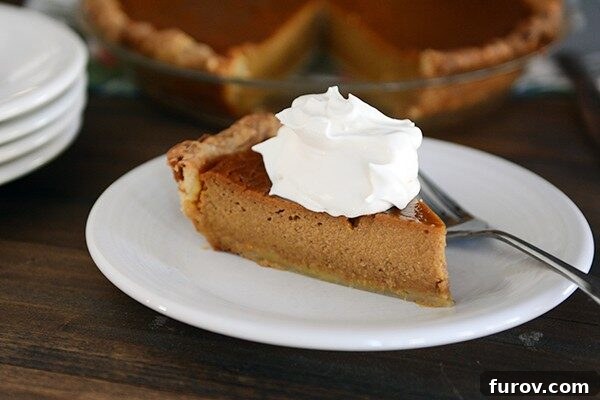 A perfect slice of classic pumpkin pie topped with a generous swirl of whipped cream, ready to be enjoyed.