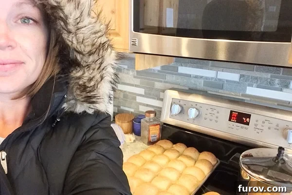 A person, bundled in a winter parka, baking homemade rolls in an oven, using the residual heat to warm up a cold house during a heating outage.