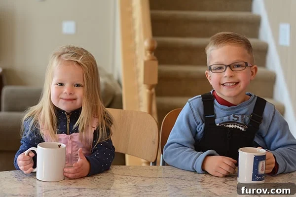 A young boy and girl happily drinking hot chocolate indoors, bundled in warm clothes after playing in the snow, during a home heating outage.
