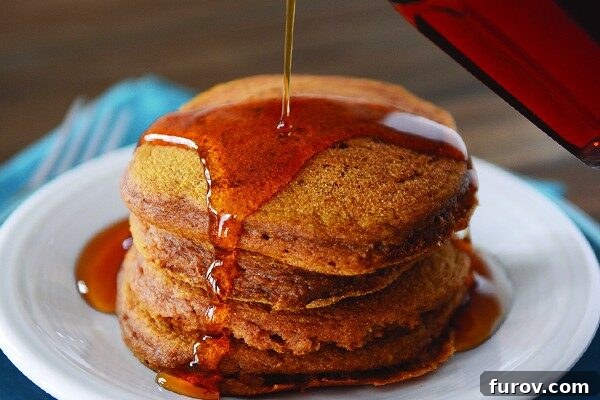 Flawless Pumpkin Pancakes 3 A stack of pumpkin pancakes getting syrup poured over them.