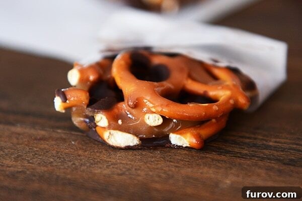 Homemade Dark Chocolate Sea Salt Caramel Pretzel Bark 3 A large chunk of dark chocolate sea salt caramel pretzel bark delicately wrapped in parchment paper, showcasing its rich layers.