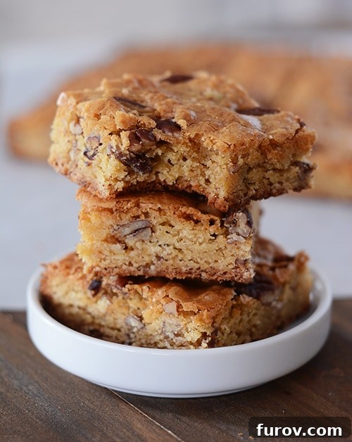 Decadent White Chocolate Pecan Brownies 2 A stack of perfectly cut white chocolate pecan brownies in a white ramekin, showcasing their chewy texture and golden-brown crust.
