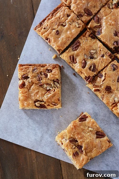 Decadent White Chocolate Pecan Brownies 4 Neatly cut white chocolate pecan brownies arranged on a piece of parchment paper, ready to be served or stored.