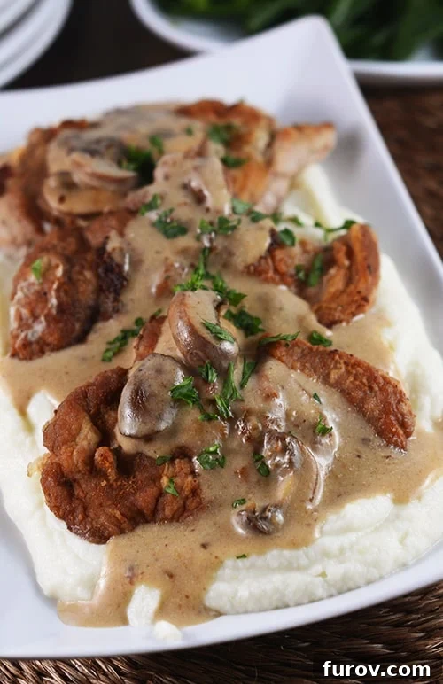 Smothered Golden Pork with Velvety Cauliflower Mash 2 Crispy pork cutlets served over creamy mashed potatoes, generously covered in a rich mushroom gravy.