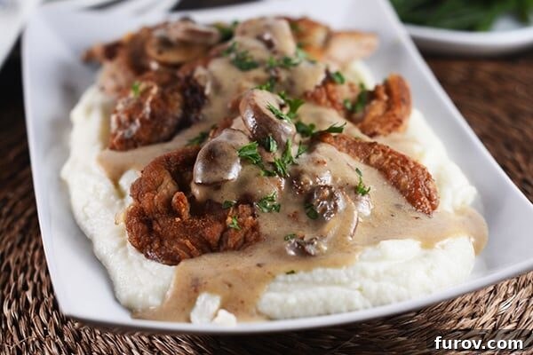 Smothered Golden Pork with Velvety Cauliflower Mash 3 Crispy pork cutlets on a bed of creamy mashed potatoes, covered with a rich brown mushroom sauce.