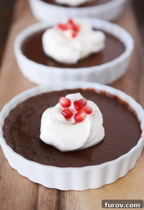 Decadent Chocolate Custard 2 Three white ramekins filled with cooked chocolate pots de creme, and topped with whipped cream and pomegranate seeds. A dark, rich chocolate dessert, perfect for entertaining.