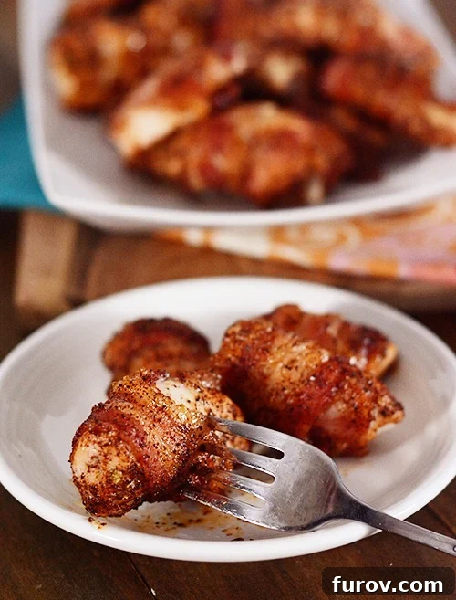 Anytime Bacon Chicken Bites 3 A fork lifts a glistening bacon-wrapped chicken bite from a plate full of appetizers, ready to be enjoyed.