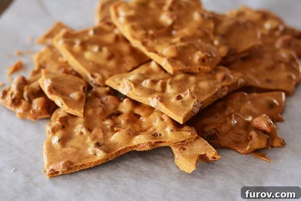 Pieces of maple cashew brittle broken apart on a piece of parchment paper, showing the golden texture and embedded cashews.