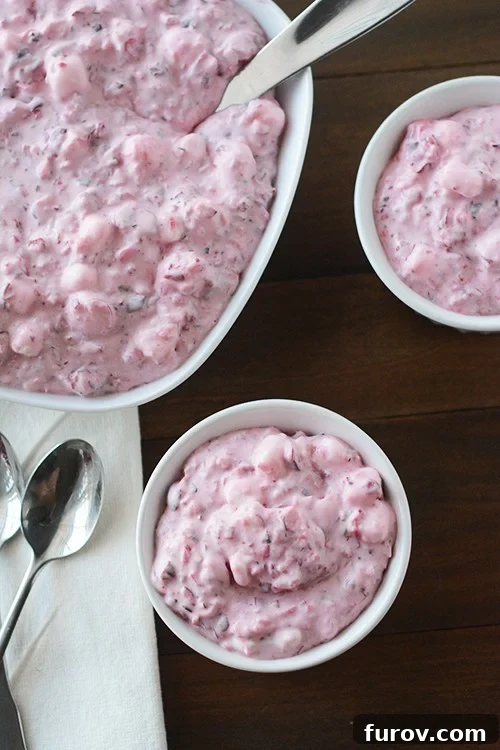 Top view of a big dish and two smaller bowls of creamy cranberry fluff salad, garnished with fresh cranberries.