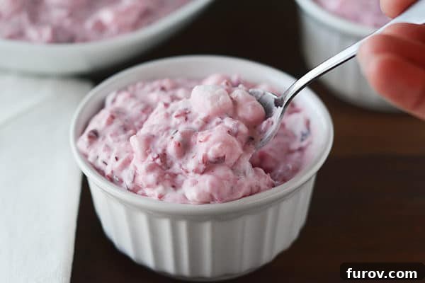 A white ramekin of cranberry fluff salad with a serving spoon nestled within.