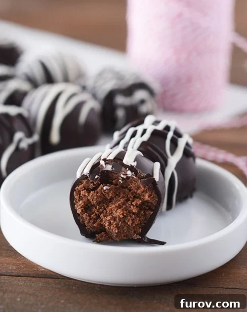 Spiced Gingerbread Chocolate Chip Cake Truffles 2 A white plate with a half-eaten chocolate gingerbread truffle revealing its moist interior, and a whole truffle behind it.