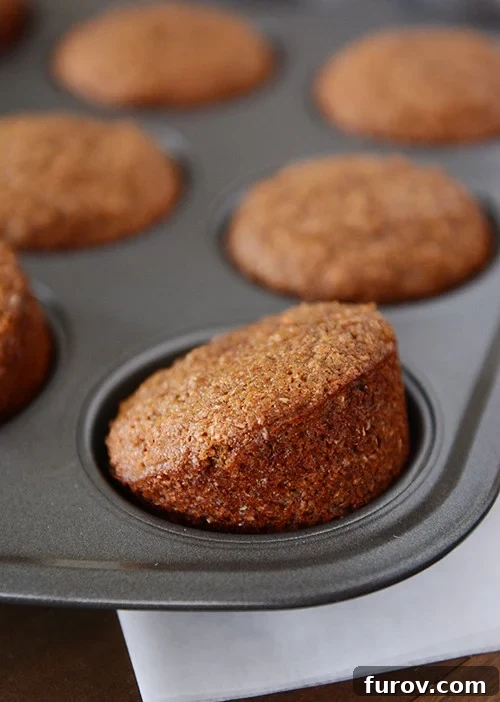 Golden brown Whole Grain Honey Bran Muffins fresh from the oven, arranged in a muffin tin, with one tilted slightly to showcase its perfect dome.