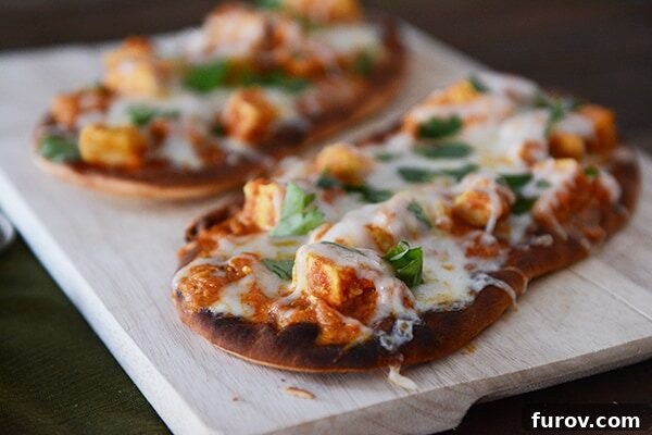 Easy 20 Minute Chicken Tikka Pizzas 3 Two freshly cooked, golden-brown cheesy chicken tikka pizzas on a wooden cutting board, garnished with cilantro and sliced red onion, ready for serving.