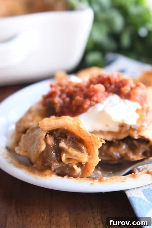 Bite of saucy enchilada on white plate with fork.