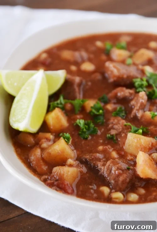 A white bowl of slow cooker beef and sweet potato stew, garnished with fresh cilantro and lime wedges on the side.