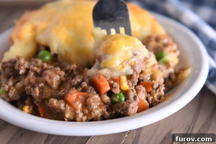 Rustic Meat and Potato Pie 9 A mouthwatering serving of Shepherd's Pie in a white bowl, with a fork digging in to reveal the perfect layers of savory beef and cheesy mashed potatoes.