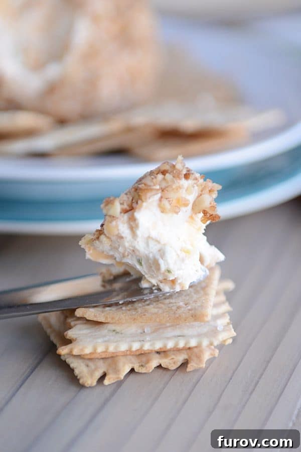 Piece of cheeseball on a knife above a stack of crackers.