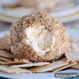 Pecan crusted cheeseball with a scoop taken out, on a plate with crackers.