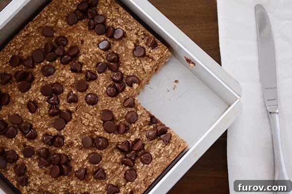 Wholesome Banana Bread Chocolate Chip Oat Bars 3 Top view of a square pan of banana oat chocolate chip bars with a piece cut out, revealing the soft interior.