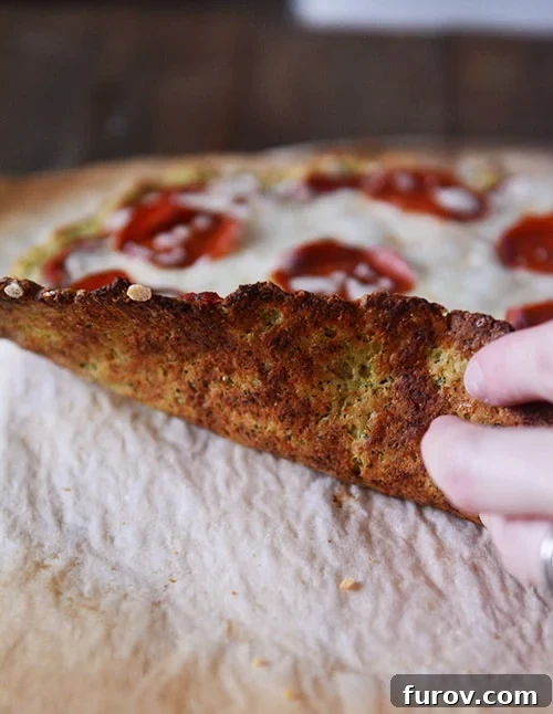 Wholesome Zucchini Pizza Base 3 A hand lifting up a pizza to show the bottom of a cooked zucchini crust.