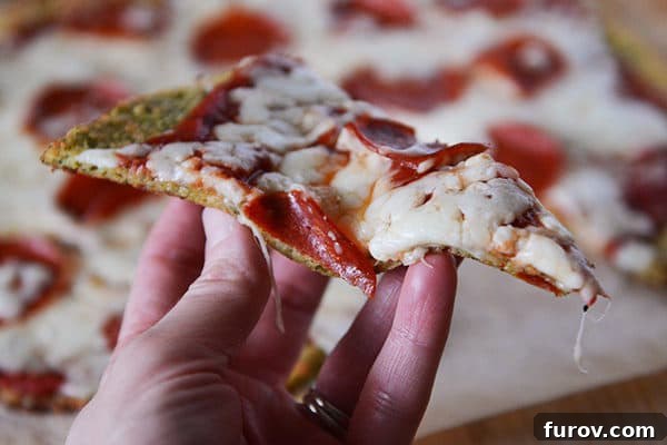 Wholesome Zucchini Pizza Base 5 Hand holding a piece of pepperoni pizza with a bite taken out.