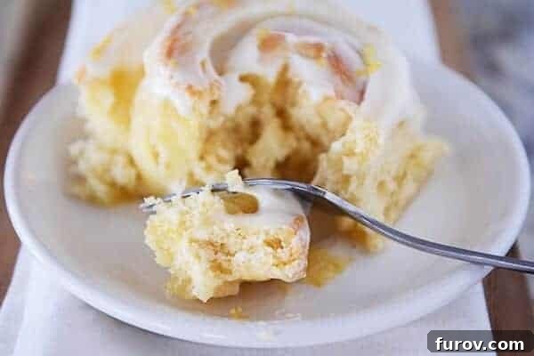 Bright Lemon Sticky Buns with Zesty Cream Cheese Glaze 3 Frosted lemon sticky bun on a white plate, with a fork taking a bite.