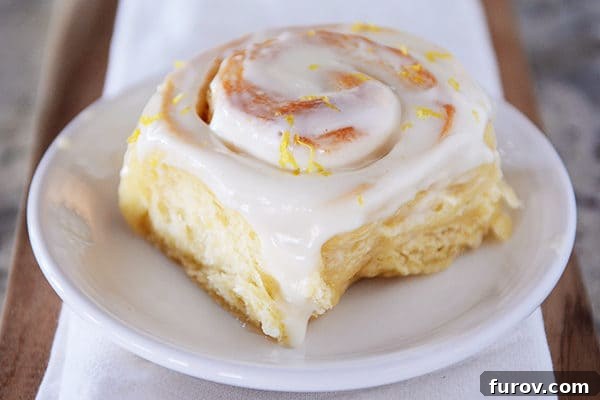 Bright Lemon Sticky Buns with Zesty Cream Cheese Glaze 4 Whole frosted lemon sticky bun resting on a pristine white plate.