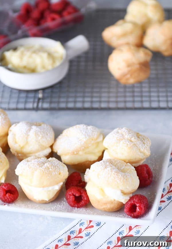 A beautiful white tray overflowing with perfectly baked, golden-brown foolproof cream puffs, garnished with fresh, vibrant raspberries.