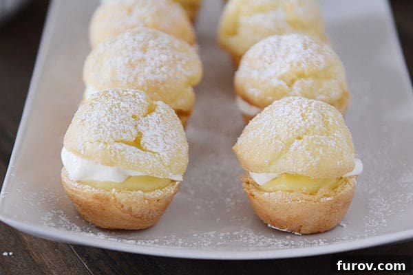 A elegant white platter holding an array of mini cream puffs, delicately dusted with powdered sugar, ready for serving.